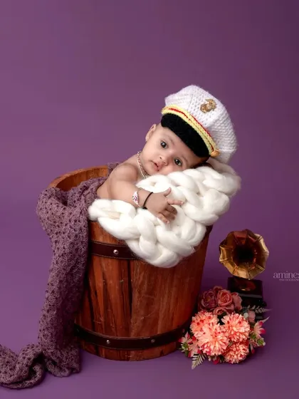 Ahoy, captain! A cute baby wearing a sailor's cap rests in a wooden bucket. The vintage gramophone prop adds a unique, nostalgic touch to the scene.