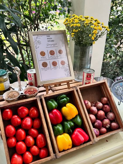 Our pizza station setup is designed to be both functional and visually appealing. We use rustic wooden crates to display fresh ingredients like tomatoes, bell peppers, and onions, with a menu showing the different pizza options available.