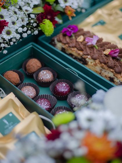 A festive green hamper filled with our handcrafted chocolate truffles and a rich chocolate loaf cake, surrounded by fresh flowers.