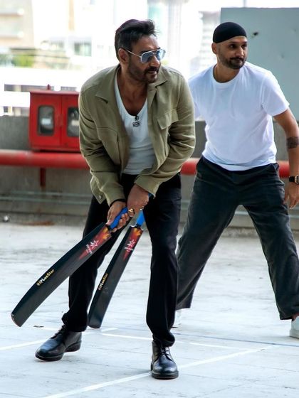 A fun, candid moment on the cricket pitch, with Ajay Devgn holding bats and sharing a laugh with Harbhajan Singh.