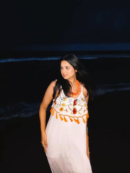 The same white dress shot against the dark waves at night. It shows how a versatile piece can work for both day and night looks on a beach vacation.