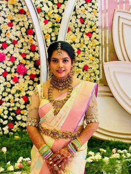 A formal portrait of the bride against a floral backdrop. Her pastel saree and traditional jewelry create a look of timeless elegance.