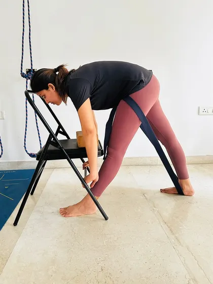We use props like chairs and straps to help you access poses safely and effectively. Here, a student uses a chair for support in Parsvottanasana (Pyramid Pose), allowing for a deeper hamstring stretch while maintaining correct alignment.