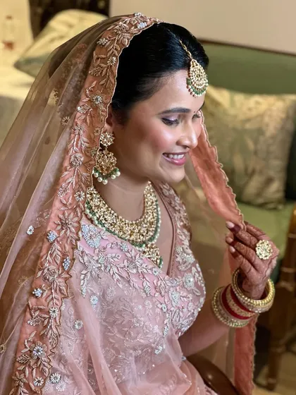 This bride is ready to say 'I do'. Her makeup is soft and radiant, and her hair is styled in a beautiful bun with fresh flowers, perfectly complementing her pastel lehenga.