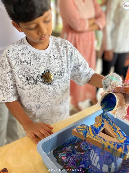 A young boy carefully pours layers of blue and yellow paint, watching as the colors merge and create incredible patterns on his wooden letter.