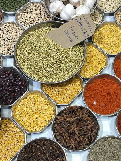 A beautiful flatlay of various dals, beans, and whole spices like star anise, arranged in steel bowls.