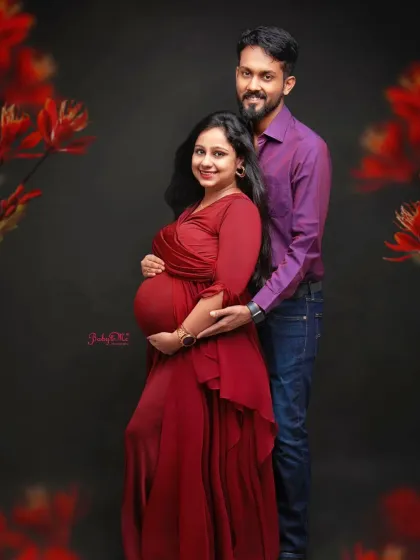 A bold and beautiful maternity portrait. The rich red gown stands out against the dark backdrop, framed by delicate red flowers for a dramatic effect.