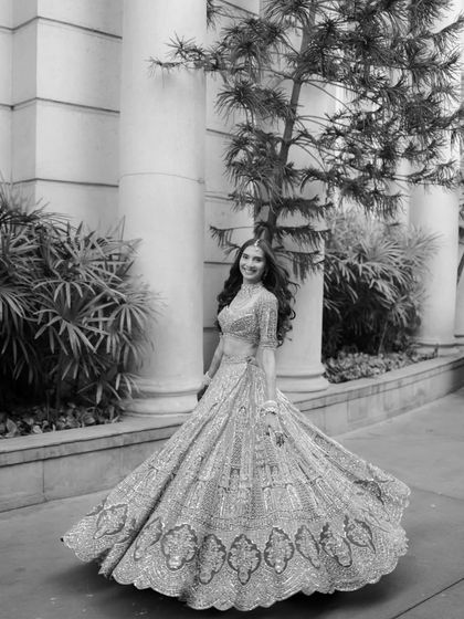 A joyful black and white shot of the bride twirling, her lehenga creating a beautiful shape against the classic architecture.