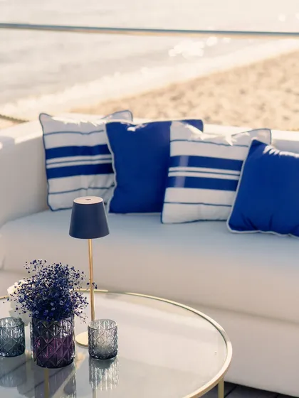 A close-up of the lounge seating, showing the crisp blue and white cushions and a small table with delicate floral arrangements, right by the water's edge.
