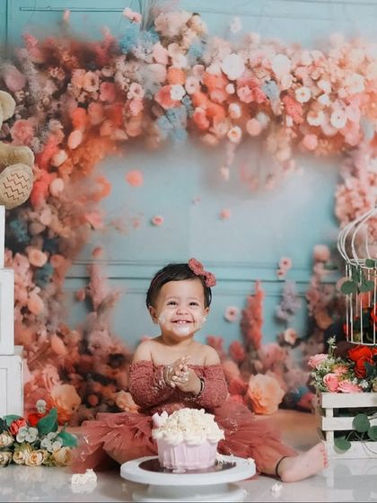 The birthday girl claps her hands in delight in front of her cupcake. The floral theme, complete with teddy bears and a birdcage, creates a fairytale atmosphere.