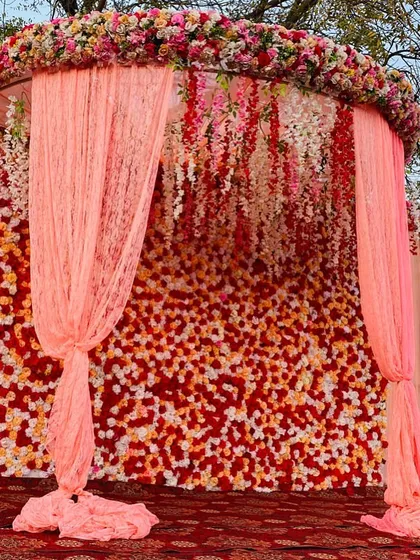 A beautiful photo backdrop featuring a wall of red, orange, and white flowers, with elegant pink drapes.