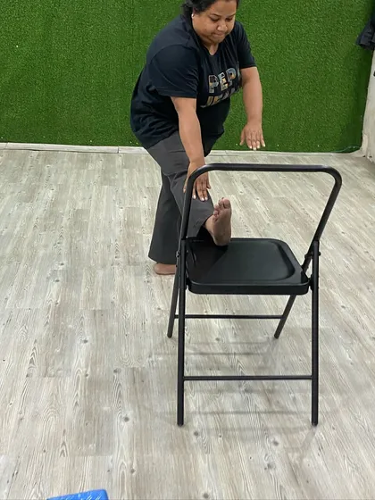 A gentle hamstring stretch using the chair for support and balance.