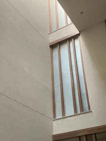 A tall, narrow window set within a double-height space. The wooden fins provide privacy and modulate the light, while the verticality of the window emphasizes the height of the room.