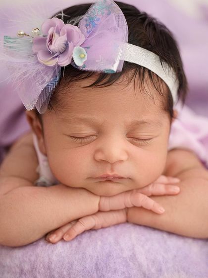 A beautiful close-up focusing on a newborn's face, highlighting their perfect features and a lovely purple floral headband.