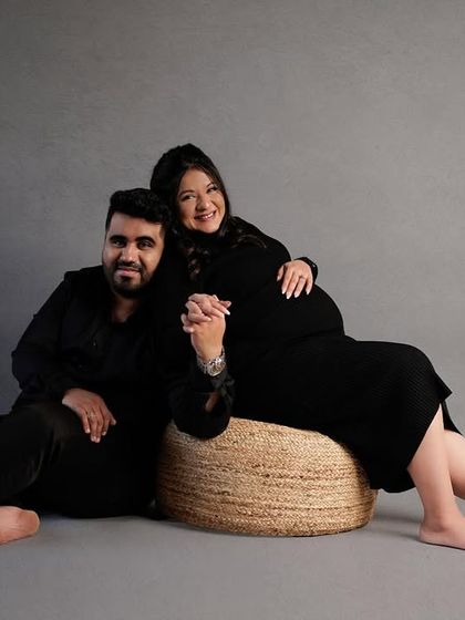 A relaxed and happy portrait of a couple in matching black outfits, seated in our modern studio setup.