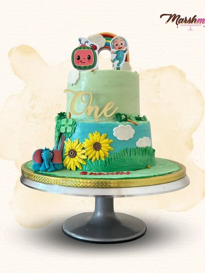 A sweet Cocomelon-themed cake for a first birthday. This two-tiered design features a gentle green and blue landscape with sunflowers and a cute, edible elephant.