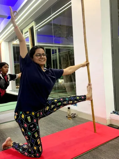 A student joyfully uses a bamboo stick for balance in this standing pose. Our classes are not just about intensity; they are also about finding joy in movement.