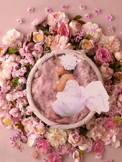 An overhead shot of a newborn angel sleeping in a basket surrounded by a circle of pink flowers.