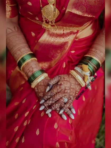 The bride's hands, adorned with a dark and beautiful mehendi stain, resting against her traditional red wedding sari. A perfect picture of bridal elegance.