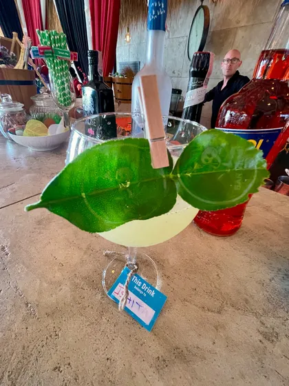 A cocktail garnished with a kaffir lime leaf, clipped on with a miniature clothespin. The leaf imparts a beautiful citrus aroma, and the branded tag adds a personalized touch for the guest.