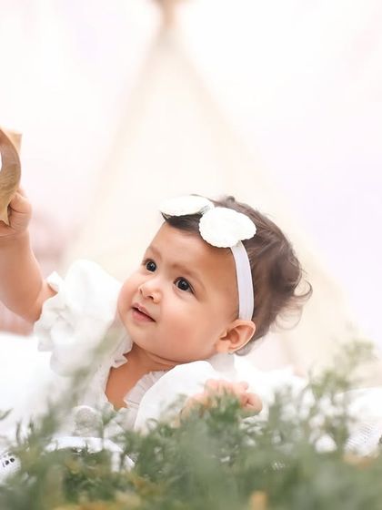 A moment of pure curiosity as the baby girl lies on her tummy and examines a leaf. This close-up from her first birthday session captures the simple wonders of childhood.