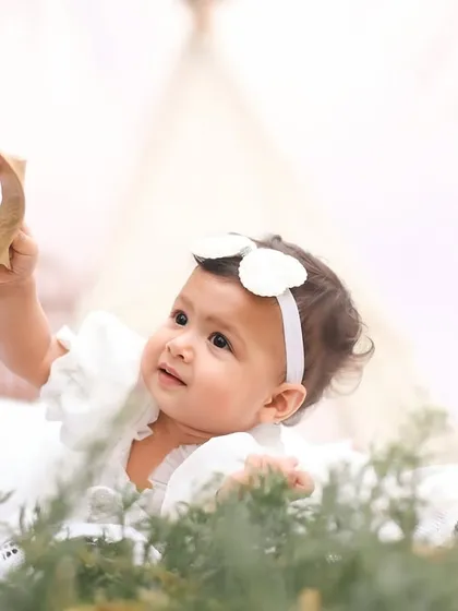 A moment of pure curiosity as a little girl in a white dress examines a leaf. The soft, bright lighting gives this outdoor portrait an angelic feel.