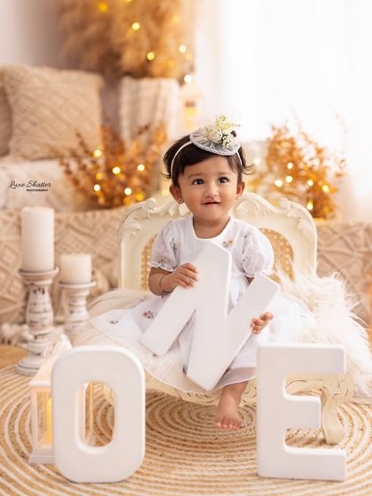 A sweet baby girl holds the letter 'N' from our "ONE" sign in a cozy, boho-themed first birthday setup.