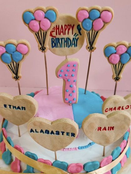 This cake was designed for four siblings. It features a pink and blue theme and has four separate heart-shaped cookies, each with a different name.