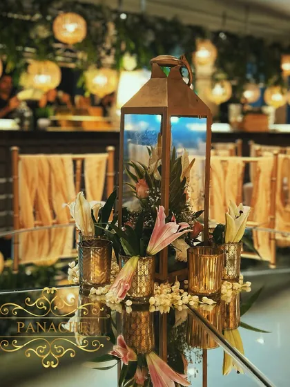 A close-up of the centerpiece, featuring a floral arrangement inside a rustic gold lantern, surrounded by smaller votives. This creates a warm and intimate ambiance.