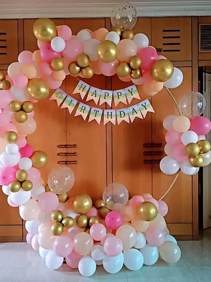 A lovely balloon ring in pastel pink, white, and gold. A 'Happy Birthday' banner is strung across the center, making it a perfect photo backdrop for a home celebration.