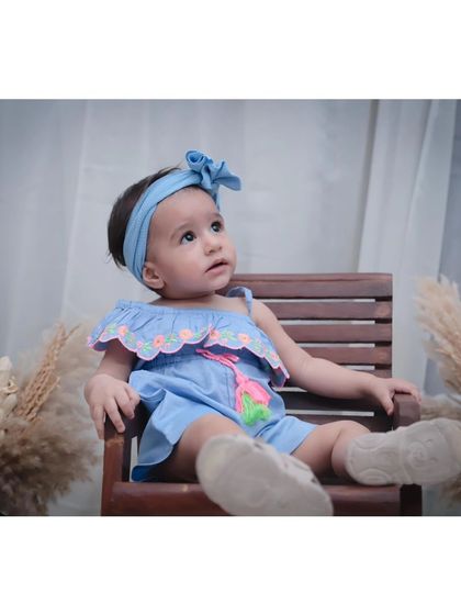 A baby girl sitting on a small wooden bench, looking thoughtful. We use simple props to create classic, timeless portraits.