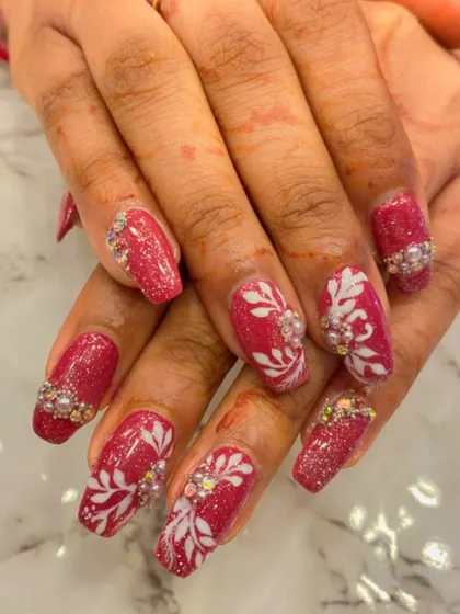 Perfect for weddings and festive events, this design combines deep red glitter nails with intricate white floral patterns. The look is elevated with 3D pearl and crystal embellishments for a touch of glamour.