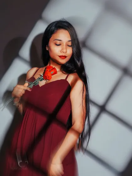 A soft and romantic pose, looking down at the rose. The shadow play across her face and dress adds depth and a dreamy quality to the image.
