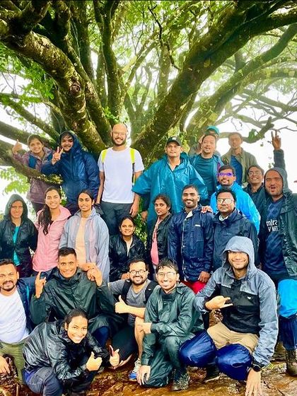 A large group under a magnificent tree, all in ponchos. This photo captures the beauty of trekking in the monsoon with a great team.