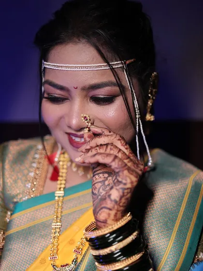 A close-up of the bride, shyly adjusting her nath. This shot highlights the intricate details of her makeup and jewellery.