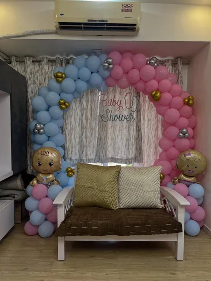 A classic "He or She" themed baby shower decoration. This setup features a beautiful balloon arch with distinct pink and blue sections, accented with baby-shaped foil balloons to create a perfect photo spot for the parents-to-be.