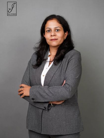A classic corporate headshot against a solid grey background. The subject's grey suit and arms-crossed pose create a look of formal authority.