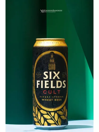 A close-up of a Six Fields Cult beer can, with condensation droplets highlighting its refreshing quality. The strong geometric background and lighting make the product label pop.