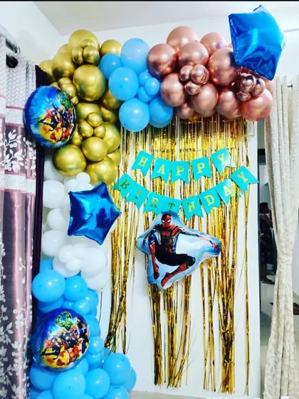 A compact yet exciting Spider-Man themed birthday decoration for a home. The setup uses a gold tinsel curtain with a blue, gold, and white balloon garland and Spider-Man foil balloons.