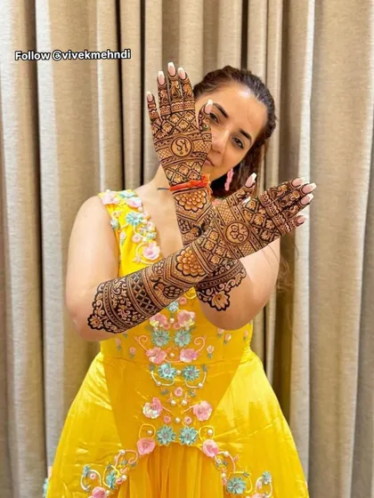 A lovely shot of a bride in her yellow mehndi outfit, with her hands crossed to show the detailed patterns and initial monograms.