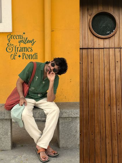 A self-portrait while sitting on a bench in Pondicherry, next to a beautiful wooden door with a porthole window set in a mustard-yellow wall.