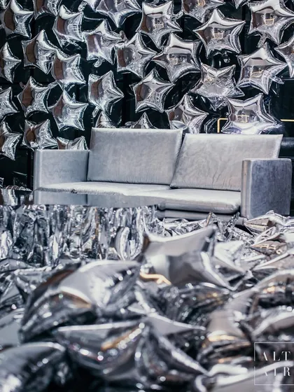 A photo booth moment from 'The Melting Disco Ball', featuring a wall of silver star balloons and a floor covered in confetti. Every corner of this event was designed to be an immersive, high-glam photo opportunity.