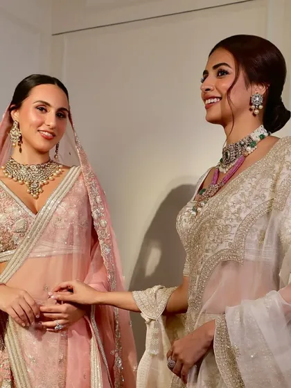 A candid moment between two brides, one showcasing a maximalist stacked necklace and the other a delicate polki choker.
