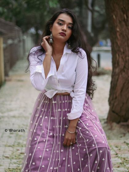 A stylish outdoor portrait combining a casual white shirt with an elegant skirt. The street setting gives it a modern, lifestyle feel.