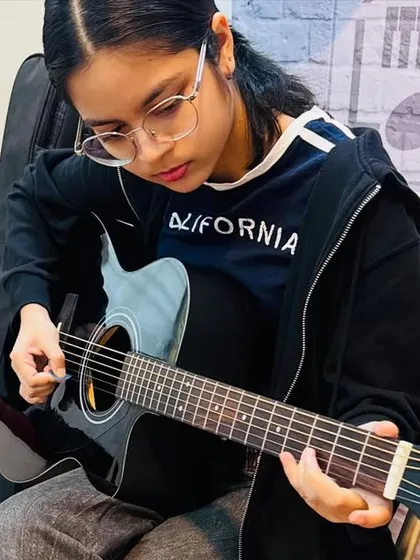 Focus and precision are key. This student is deep in concentration, practicing her fingerpicking technique on an acoustic guitar, an essential skill for any aspiring guitarist.