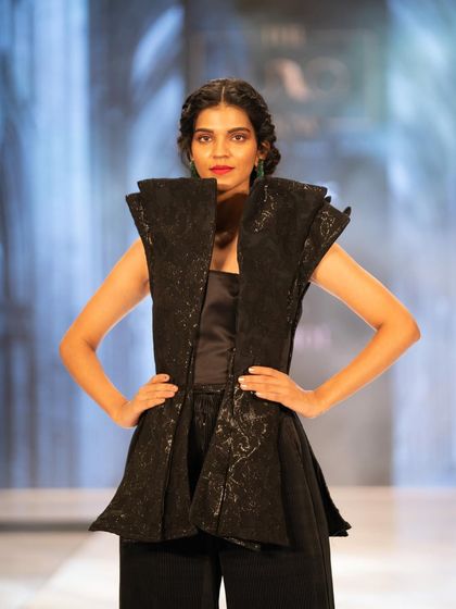 A strong, structured look from The Luxo Show. The makeup features a classic red lip and clean skin, allowing the architectural design of the outfit to stand out.