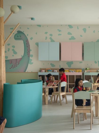 Pastel-colored storage cabinets and a dinosaur mural in the nursery library. This area provides a space for more structured activities like drawing or group reading, complementing the free-form play zones.