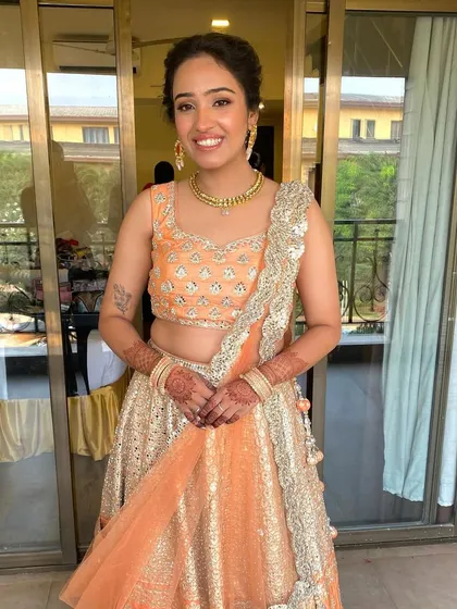 A full-length shot of the groom's sister. Her peach lehenga is beautifully complemented by the soft and radiant makeup.