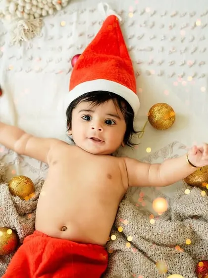 Making a little snow angel! This playful shot of a baby in a Santa hat, lying amongst fairy lights and ornaments, is full of festive fun and charm.