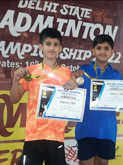 A close-up shot of our Delhi State Champions, Arjun and Vatsal, holding their gold medals and certificates after winning the U-11 Boys Doubles title.